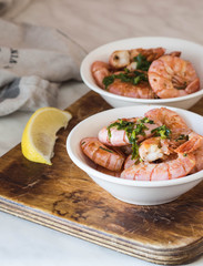 Two white bowls with shrimps fried with herbs and garlic on an old board on a white table
