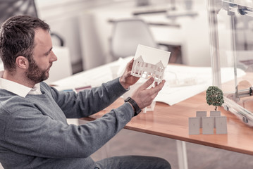 Beautiful layout. Concentrated bearded man working on landscape design project making model of house