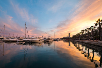 Fototapeta na wymiar Beautiful port of Alicante, Spain at Mediterranean sea. Luxury yachts, ships, ferries and fishing boats sailing and standing in rows in harbor. Rich people traveling around the world. Sunset evening