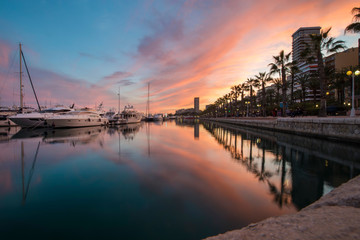Beautiful port of Alicante, Spain at Mediterranean sea. Luxury yachts, ships, ferries and fishing boats sailing and standing in rows in harbor. Rich people traveling around the world. Sunset evening