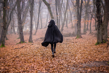 Girl in black hood running away from danger deep in dark forest. Thick fog all around. Scary autumn scene