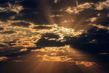 Dramatic sky with dark clouds and orange rays of the sun at sunset