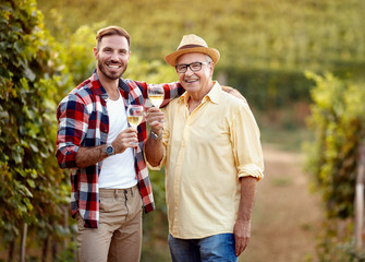 smiling father and son tasting wine in vineyard.