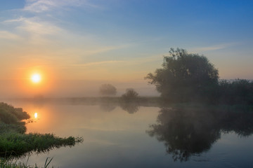 Orange sun over river surface with fog in summer morning. River landscape