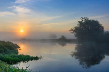 Fototapeta na wymiar Orange sun over river in early morning. Summer river landscape