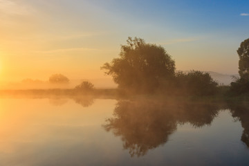 Orange sunrise over river surface with fog in early summer morning. River landscape