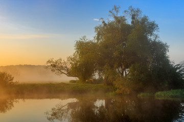 Fototapeta na wymiar Orange sunrise with fog over river surface against blue sky. River landscape in summer morning