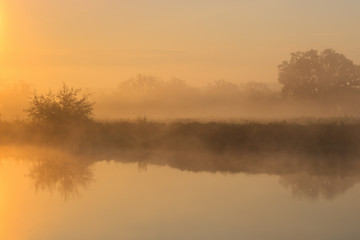 Orange sunrise over river surface with fog. River landscape in summer morning