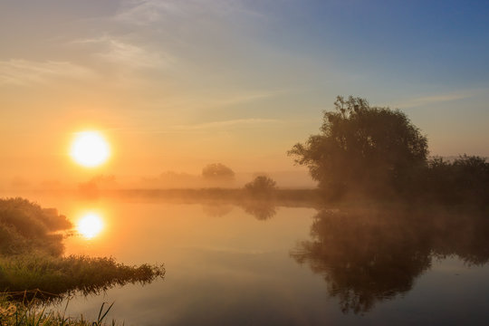 Orange sunrise over the river in fog. River landscape in summer morning