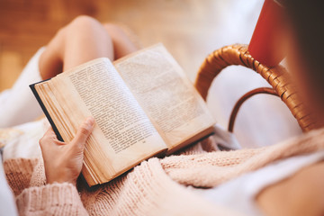 Soft photo of woman in a wicker chair with old book and cup of coffee