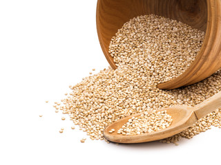 Overturned wooden bowl with quinoa seeds pouring out and a spoon next to it isolated on white background
