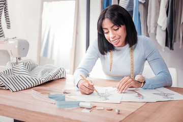 Talent. Enthusiastic positive designer drawing illustrations for clothes collection while sitting...