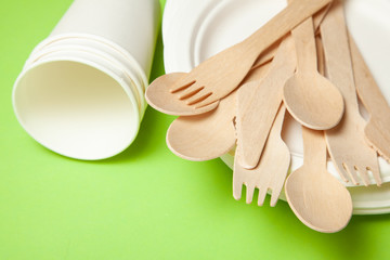 Eco-friendly disposable utensils made of bamboo wood and paper on a green. Draped spoons, fork, knives, bowls with paper cups