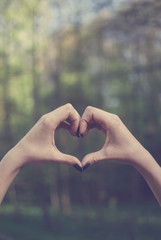 Obraz premium Girl demonstrating a heart shape gesture against spring forest covered with sunlight. Vintage retro colors