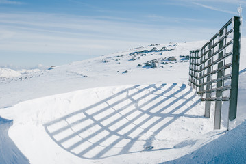 Snowy winter landscape. High wooden fence on the plateau casting shadow. Austrian Alps.