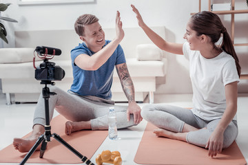 Well done. Nice smiling yoga trainers giving high five to each other sitting in front of camera