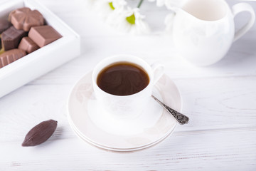 Porcelain cup of black coffee and chocolate candies on a white background