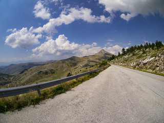 Mountain road surrounded by typical vegetation and many trees on a beautiful summer day with blue skies and few clouds