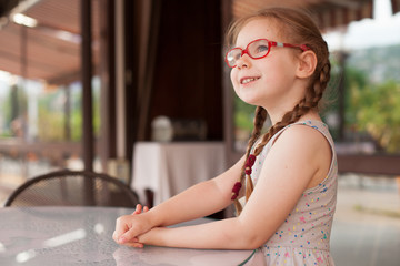 young girl with glasses and dress is sitting at a table in a cafe