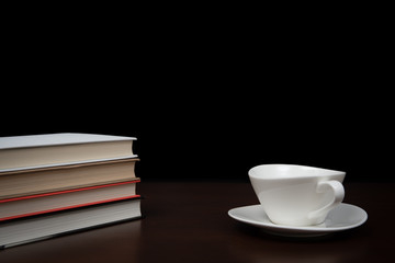 books stacked on the desk with a cup of coffee.