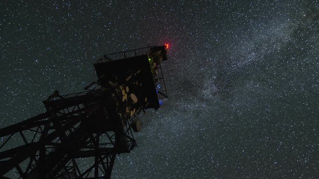 Milky way galaxy circling over communication tower in starry night sky Time lapse Zoom
