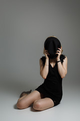 A young girl in a black dress covers her face with a hat. The beauty shy covers her face.