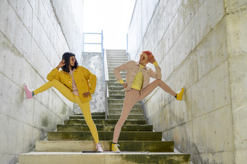 Two alternative friends posing on steps, wearing yellow and pink jeans clothes