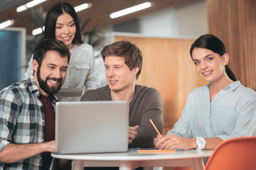 Pleasant collaboration. Joyful creative people sitting in front of the laptop while working together in team