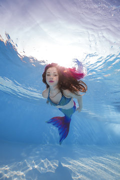 A girl in a mermaid costume poses underwater in a pool