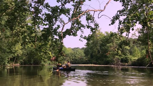 Kayaking and walking through a river and lake with stones and greenery all over. Serene nature shots with boaters and a forest.