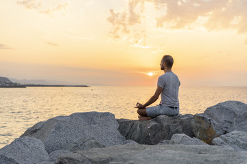 Naklejka na ściany i meble Spain. Man meditating during sunrise on rocky beach