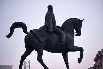 Statue of knight and horse riding towards victory. New moon, birds and plane in the background of blue night sky
