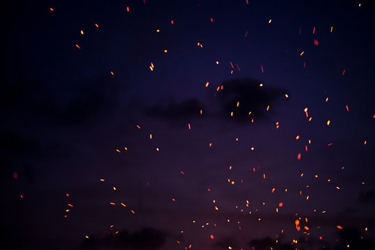 Large burning bonfire with soft glowing flame throws flying sparkles all around. Romantic summer evening, people relaxing and enjoying calmness at the seaside during the Night of ancient lights