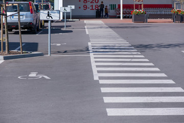 Newly made parking lot next to shopping mall in city centre with green areas and pedestrian crossing. Arrows and signs on asphalt showing rules and directions