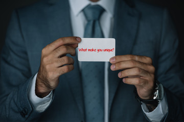 cropped view of businessman in suit holding business card with "What make you unique?" lettering