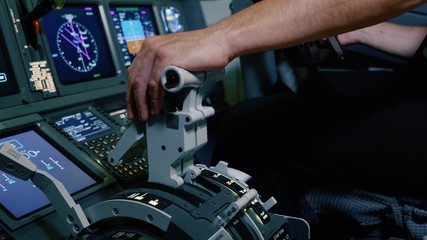 Pilot holding hand on the thrust lever handle for engine control of airliner.