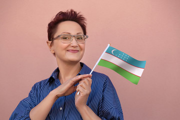 Uzbekistan flag. Woman holding Uzbekistan flag. Nice portrait of middle aged lady 40 50 years old with a national flag over pink wall background outdoors.