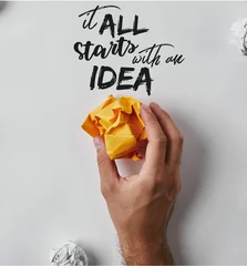 Foto op Plexiglas cropped shot of man holding crumpled yellow paper with "it all starts with an idea" inspiration on white surface © LIGHTFIELD STUDIOS