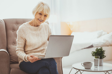 Online conversation. Amazing pensioner bowing head while holding laptop on knees