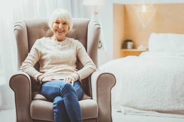 Obraz premium Happy adulthood. Beautiful mature woman sitting on armchair and posing on camera