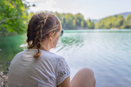 Junges M&auml;dchen sitzt am See und blickt in die Ferne