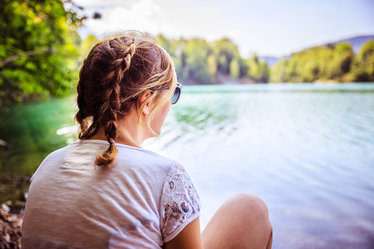 Junges M&auml;dchen sitzt am See und blickt in die Ferne