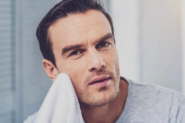 Fototapeta premium In the bathroom. Handsome mature man toweling off his face while getting ready for work in the bathroom