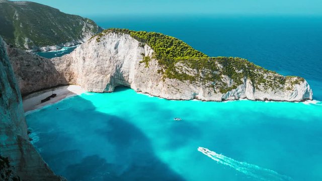 4k Timelapse of the world famous Navagio beach, Zakynthos, Greece. Turquoise sea water rolled to white sand beach with Shipwreck. Clouds shadow moving on water. Fist tourist boats arrived the bay