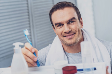 Good-looking man. Good-looking smiling man feeling relaxed while holding toothbrush after taking shower