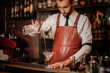 Bartender pourring cocktail with an ice cubes into the cocktail glass