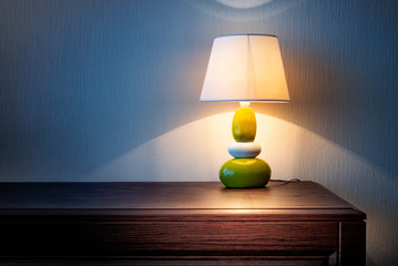 Little yellow, gray and green lamp on a wooden dresser or a night table, illuminating the wall...
