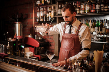 Bartender pourring a cocktail into the cocktail glass