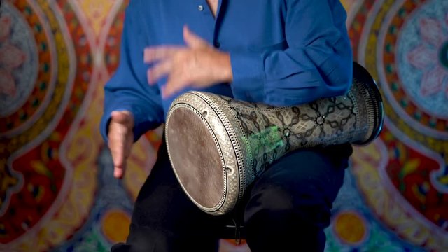 Wide shot of playing rhythms on doumbek drumming slow rhythm with arabic background.