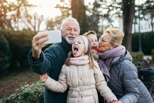 Grandparents taking selfie photo with their grandchildren in city park.